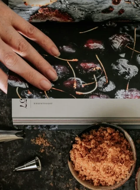 A hand turning pages in a baking book surrounded by baking supplies
