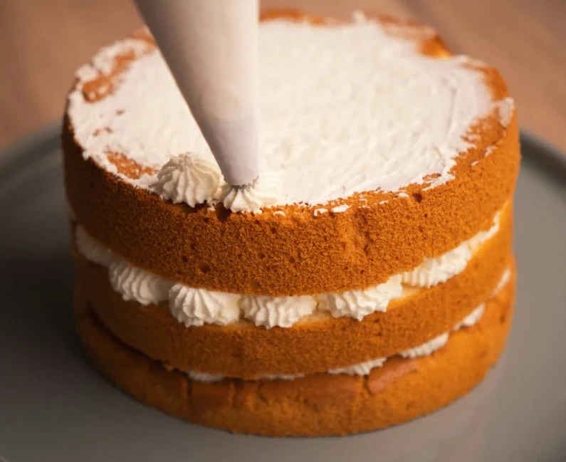 Layers of sponge cake getting topped with cream from a pipette