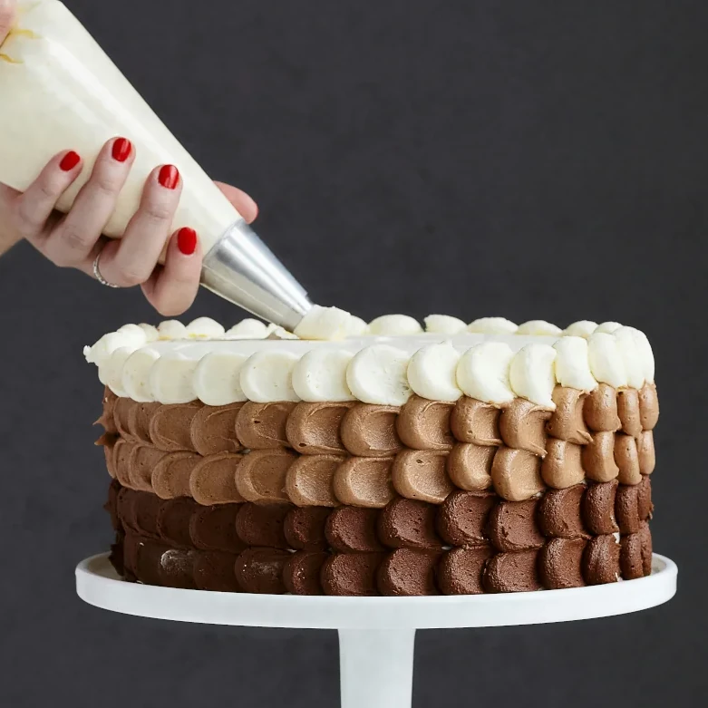 a triple chocolate cake on a platter being iced with a piping bag