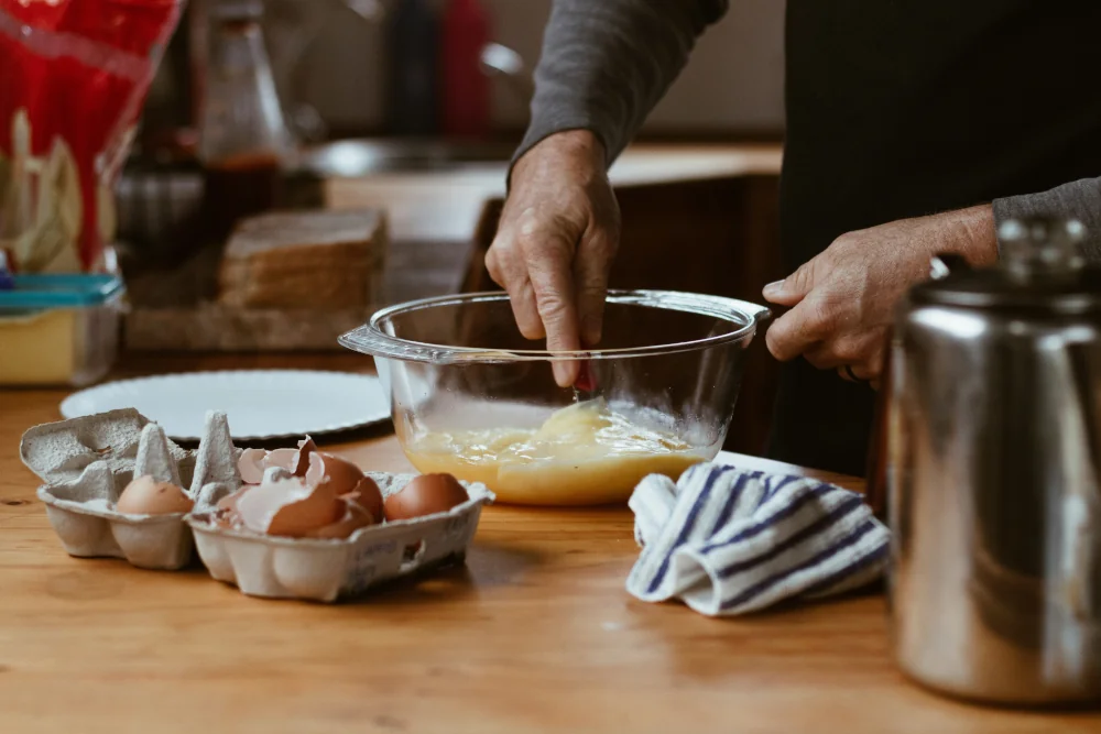 A closeup of a person in a kitchen whisking eggs in a mixing bowl